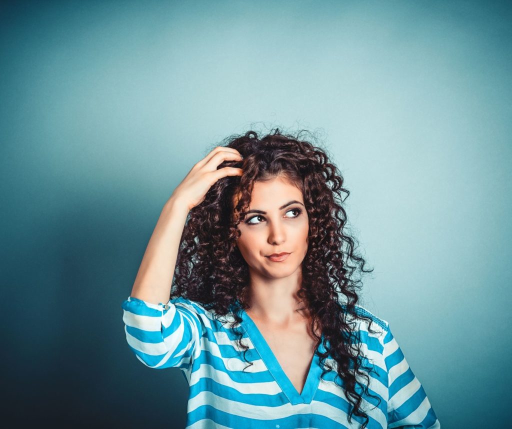A woman with curly hair scratching her head, looking thoughtful against a studio background.