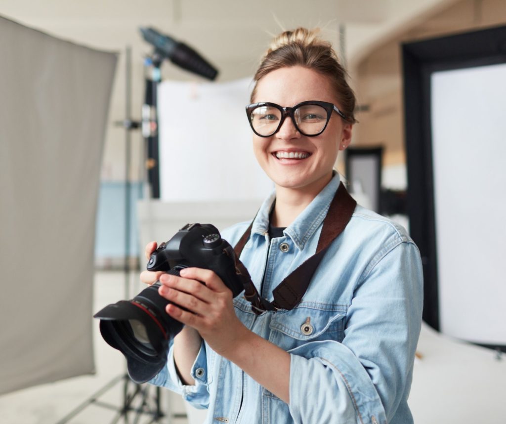 Female photographer, elliot olson, smiling and holding a camera in a studio setting.