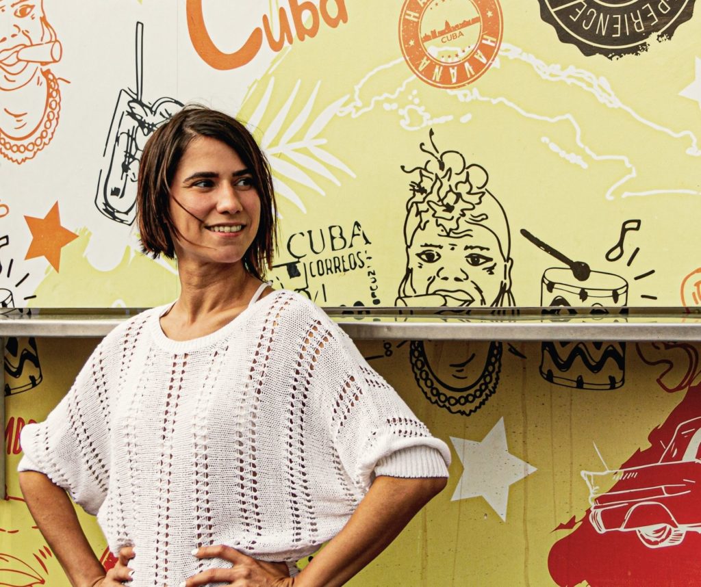 Woman smiling in front of a colorful wall with cuban-themed illustrations, captured by studio anansi in portland, oregon.