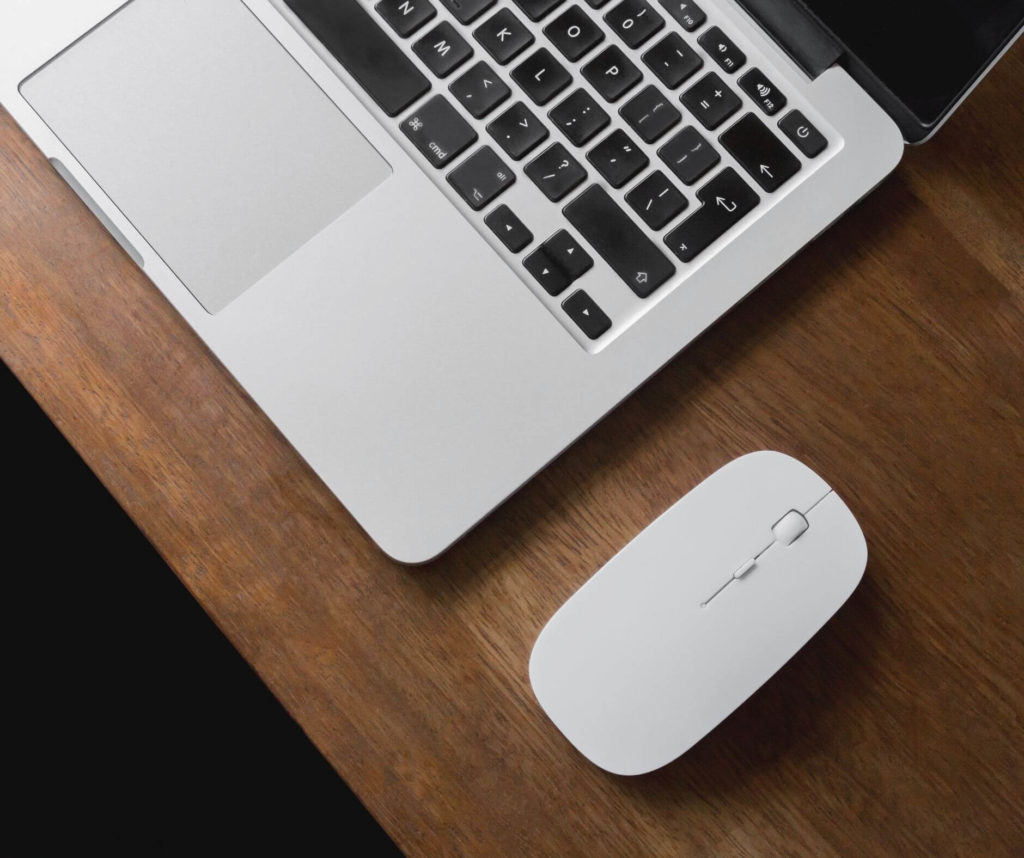 Laptop with a white wireless mouse on a wooden surface in a portland oregon studio.