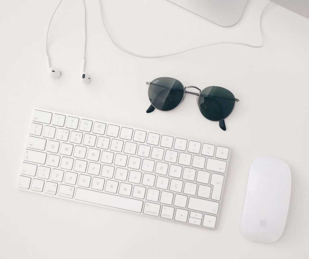 A minimalist workspace with a white keyboard, a white mouse, a pair of earphones, and sunglasses on a white desk, designed by elliot olson from portland oregon for optimal website strategy.