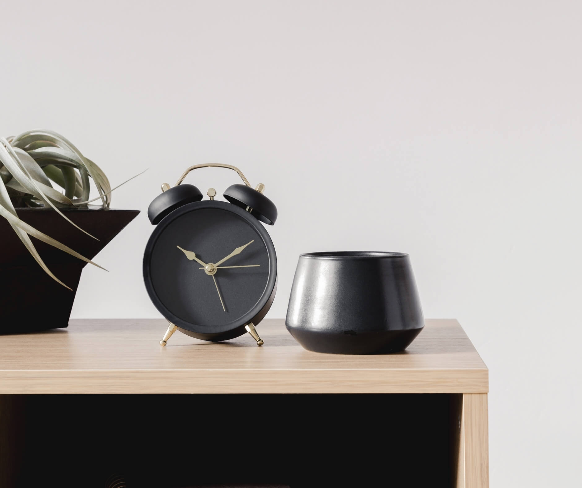 Analog alarm clock and a small plant in a pot on a wooden shelf against a neutral background, showcasing Elliot Olson's website design strategy.