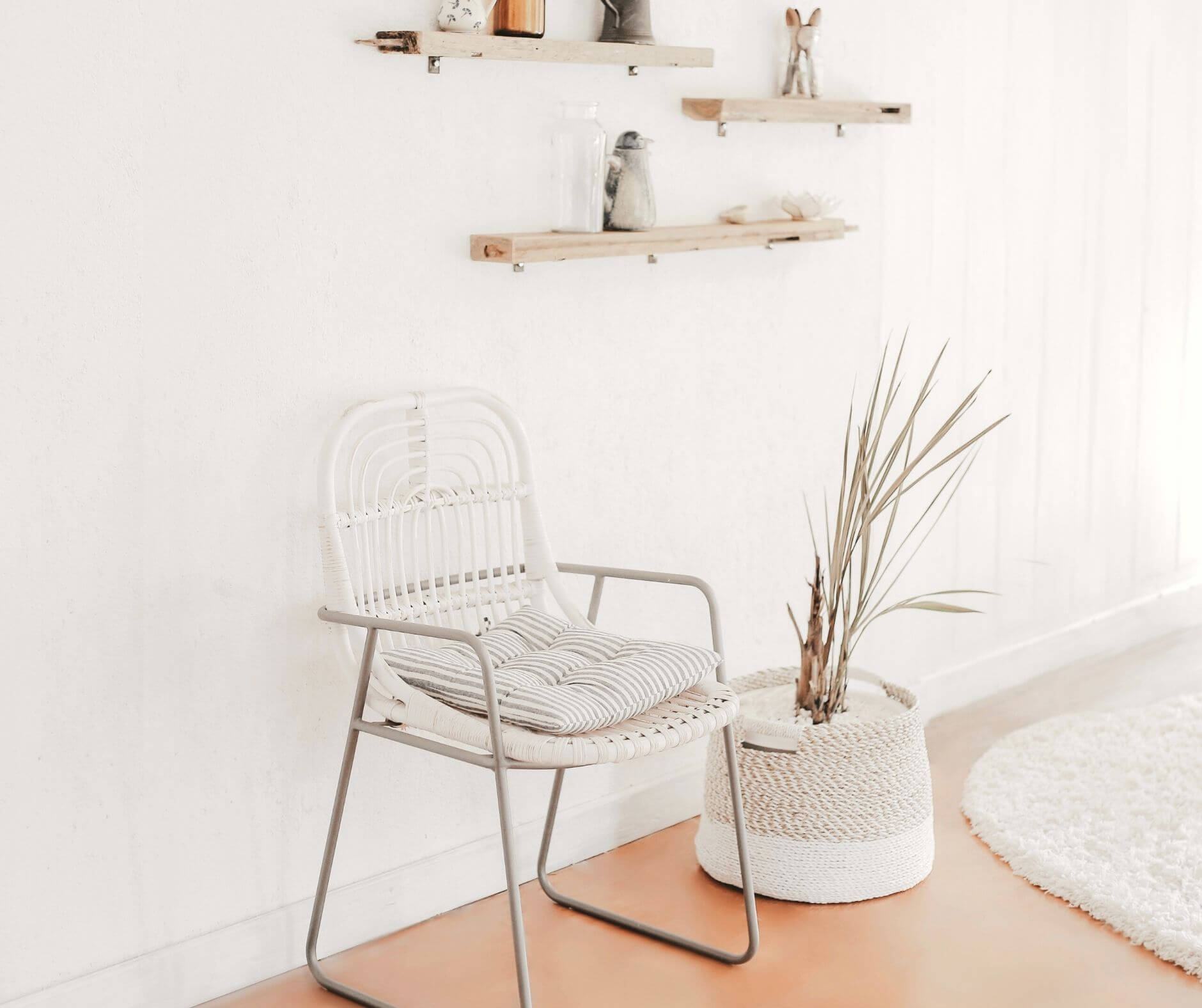 A minimalist room with a white metal chair, striped cushion, wooden shelves, and a potted plant, designed by Studio Anansi.