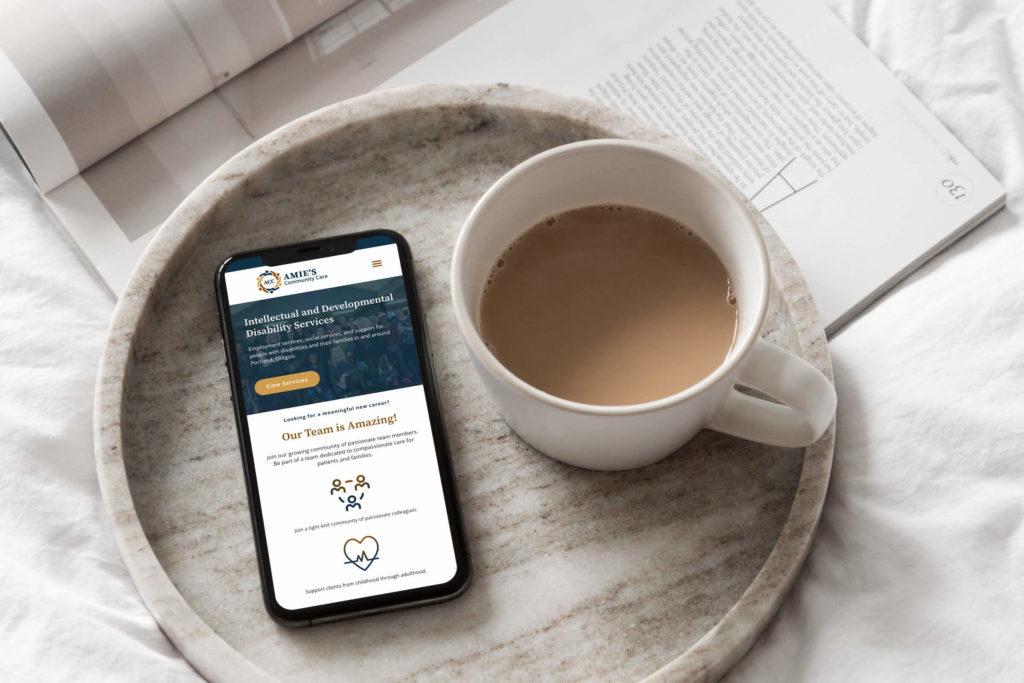 A smartphone displaying a studio anansi website next to a cup of coffee on a tray, with an open book in the background.